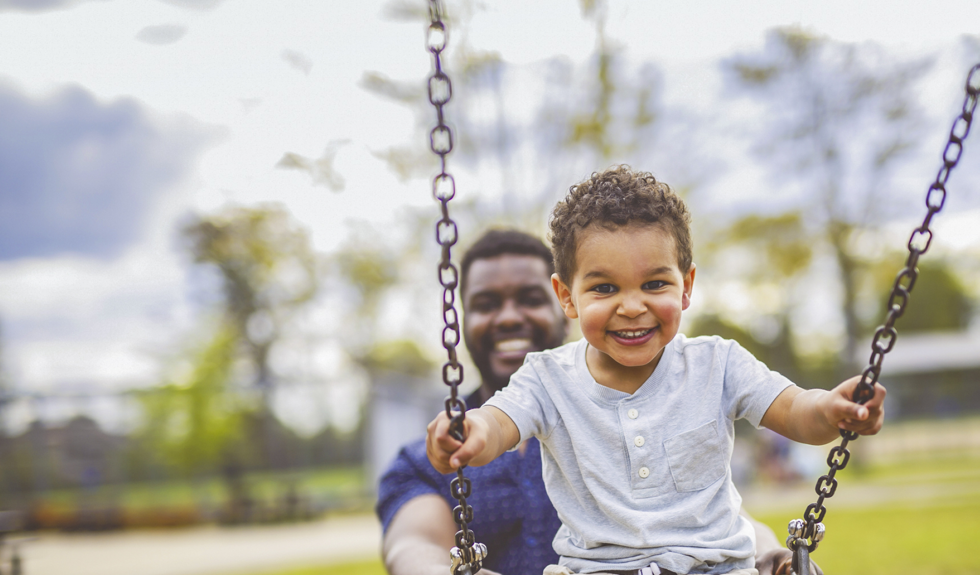Young boy on swing being pushed by a man
